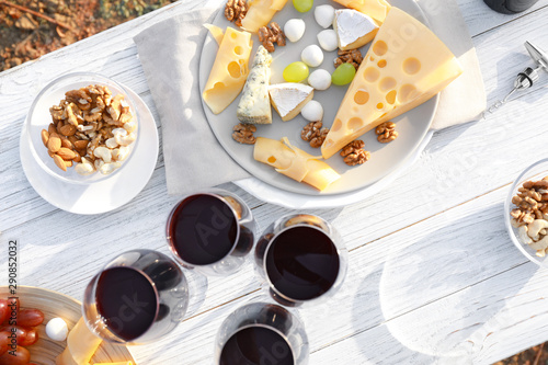 Flat lay composition with wine and cheese on white wooden table outdoors
