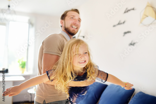 Happy young handsome father with his little curly hair daughter playing at home.