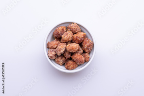 Peanuts praline sweet in a white bowl, on white background, soft light, copy space