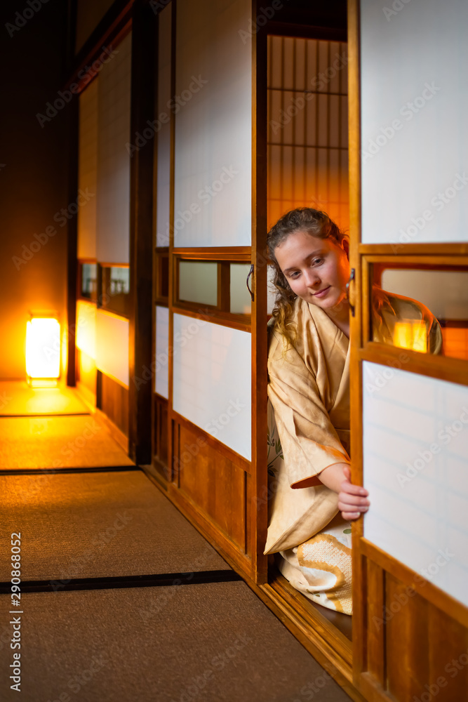 Traditional Japanese home or ryokan room with gaijin caucasian woman in kimono, tabi socks opening shoji sliding paper doors sitting on tatami mat floor Traditional Japanese home or ryokan room with gaijin caucasian woman in kimono, tabi socks opening shoji sliding paper doors sitting on tatami mat floor