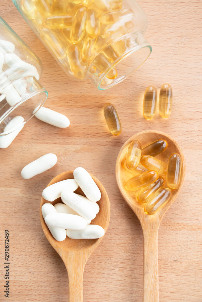 Top view of vitamin and pharmaceutical medicine pills, tablets and capsules with glass bottle on wooden background. Dietary supplement healthcare product. Concept of health. Top view of vitamin and pharmaceutical medicine pills, tablets and capsules with glass bottle on wooden background. Dietary supplement healthcare product. Concept of health.