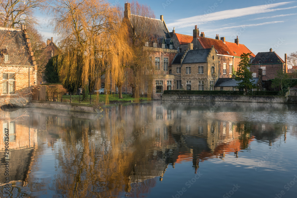 Heritage brick building with autumn tree reflect into lake in Minnewater park, Bruges, Belgium