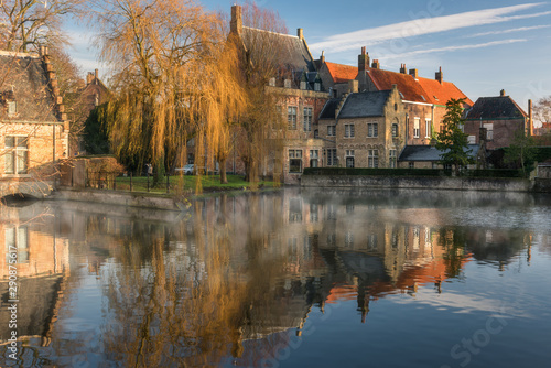 Heritage brick building with autumn tree reflect into lake in Minnewater park, Bruges, Belgium