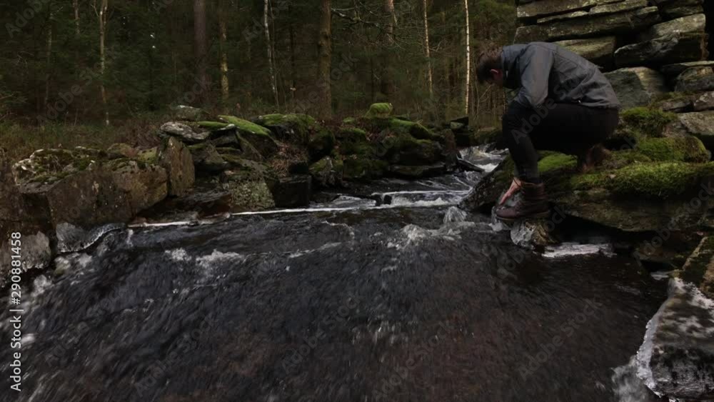 Young man sitting by a small creek running through the woods near Halland, Sweden, during winter time