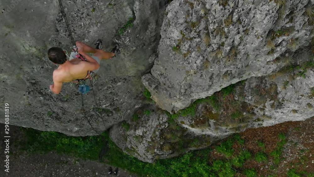 Top Down View Of Shirtless Male Climber Rappelling Down Rock Face. Aerial Pedestal Down Top Down View Of Shirtless Male Climber Rappelling Down Rock Face. Aerial Pedestal Down