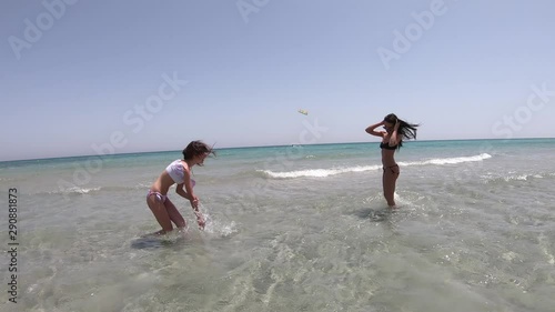 young teenage girls playing around shallow water with kite surfer in the background