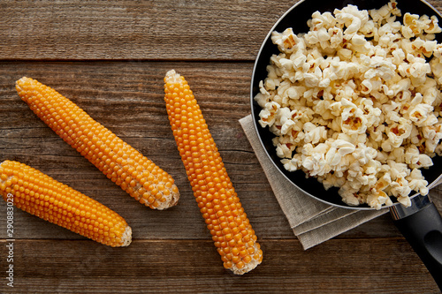 top view of delicious popcorn in frying pan near corn on wooden background