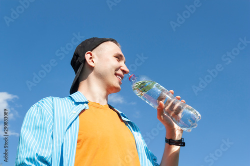 Guy drinking water from a bottle against a blue sky