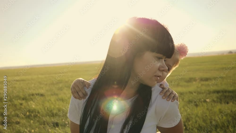 A happy family. Mom carries a beautiful little daughter on her shoulders, walking in a green field at sunset. The Concentration of Family Happiness and Joy A happy family. Mom carries a beautiful little daughter on her shoulders, walking in a green field at sunset. The Concentration of Family Happiness and Joy