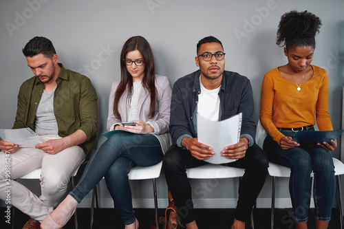 Group of multiracial young candidates waiting for interview sitting on chair holding their resumes  photo