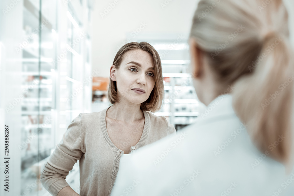 Fototapeta premium An anxiously looking picky woman attentively listening to the pharmacist.