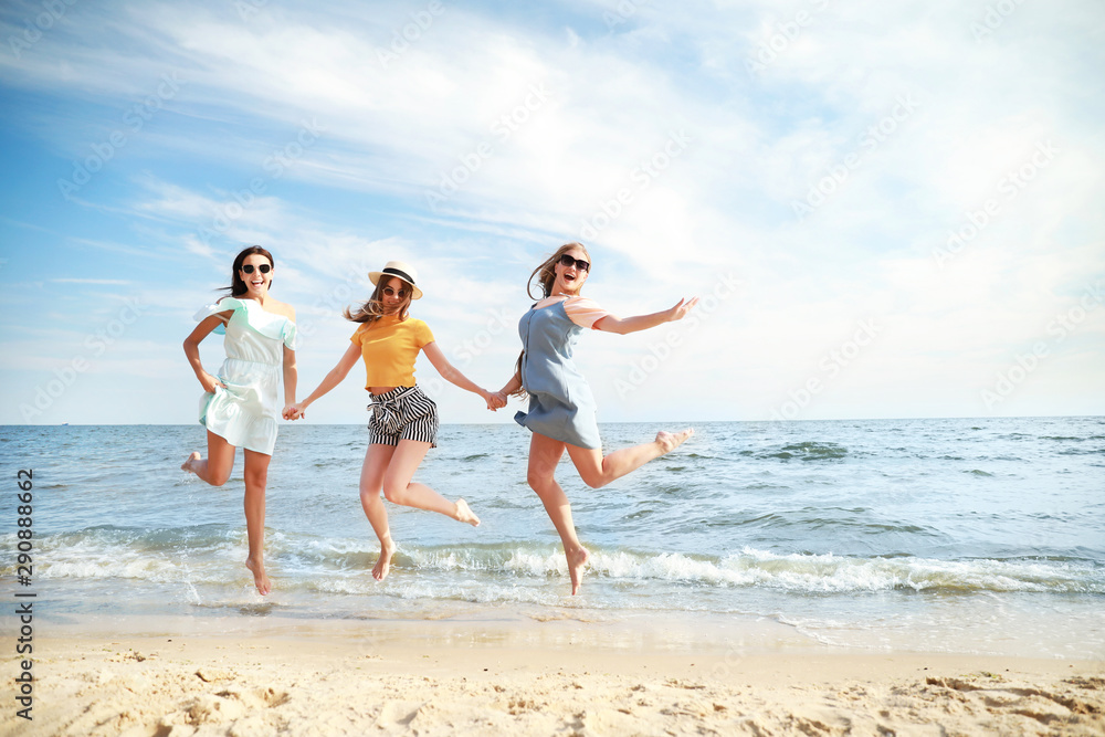 Happy jumping young women on sea beach at resort