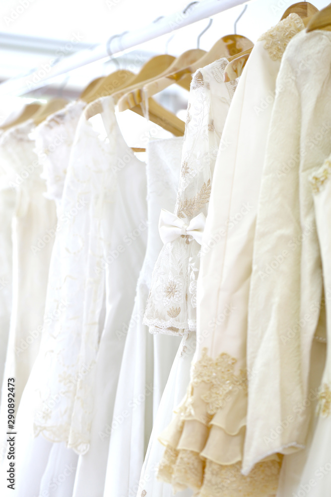 Wedding white gown for bride hanged in costume showroom for marriage or wedding reception. White delicated lace on long dress for promp or party Wedding white gown for bride hanged in costume showroom for marriage or wedding reception. White delicated lace on long dress for promp or party