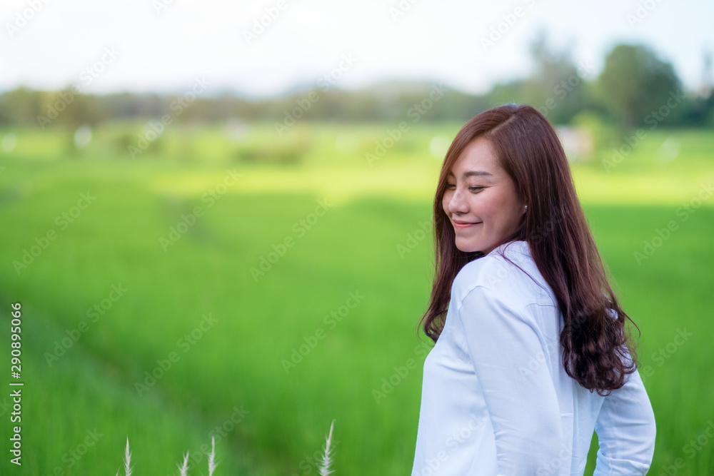 A beautiful asian woman standing in front of a green rice field with feeling relaxed and happy A beautiful asian woman standing in front of a green rice field with feeling relaxed and happy