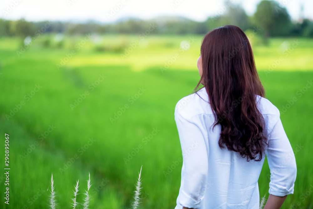 A beautiful asian woman standing and looking into a green rice field with feeling relaxed A beautiful asian woman standing and looking into a green rice field with feeling relaxed