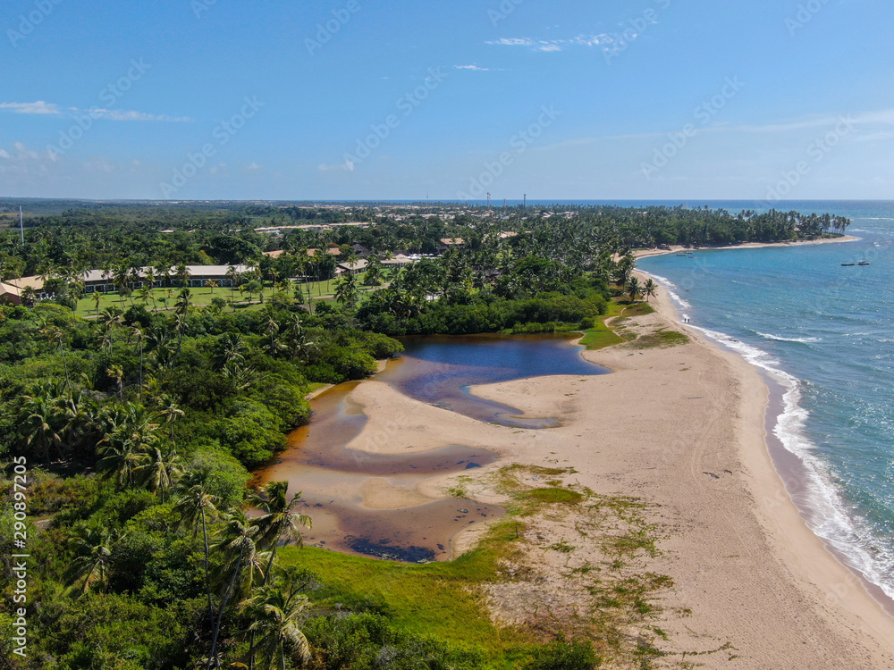 Aerial view of river merging to tropical white sand beach and turquoise clear sea water. Praia do Forte, Bahia, Brazil. Travel tropical destination
