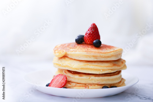 Many layers of pancake with strawberry and  blueberry on white dish  on sweet white cloth background
