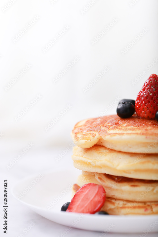 Many layers of pancake with strawberry and  blueberry on white dish  on sweet white cloth background
