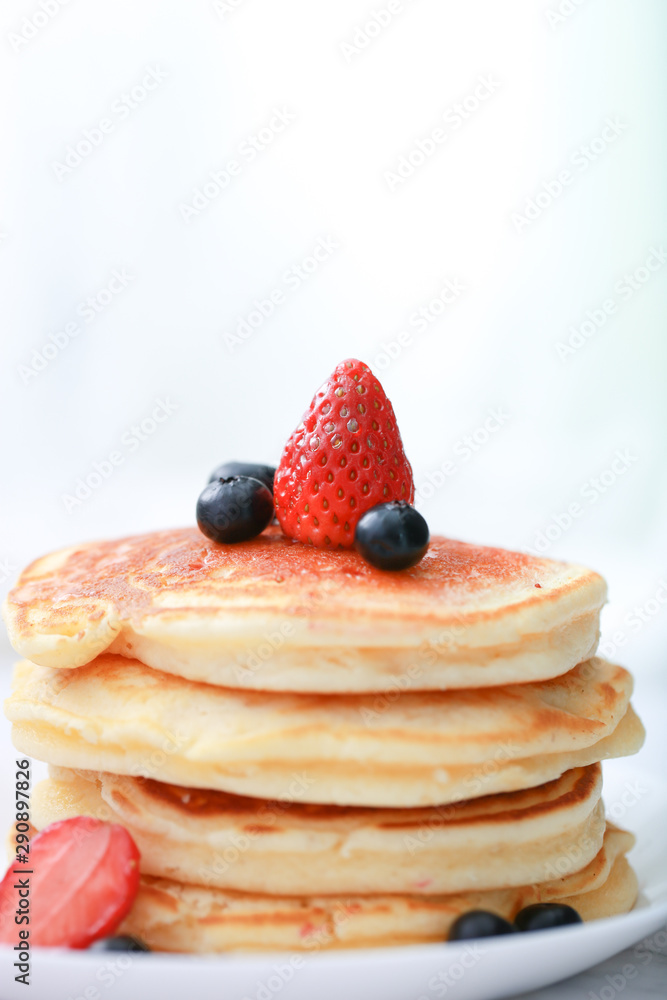 Many layers of pancake with strawberry and blueberry on white dish on sweet white cloth background Many layers of pancake with strawberry and blueberry on white dish on sweet white cloth background