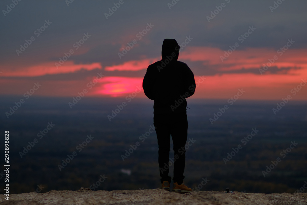 A lone man in a black jacket stands on top of a mountain in sunset time. Loneliness