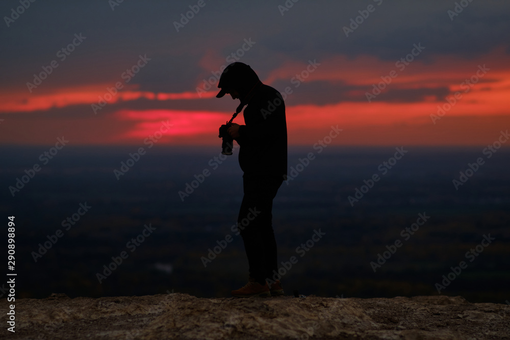 The photographer looks through photographs in his cell at sunset. silhouette of a man with a camera. Work infinity fotografia