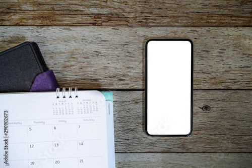 Top view of smart phone isolated white screen for mockup design or app display with calendar and note book on wooden table, tools for organize schedual and meeting. Technology and Business Concept. photo