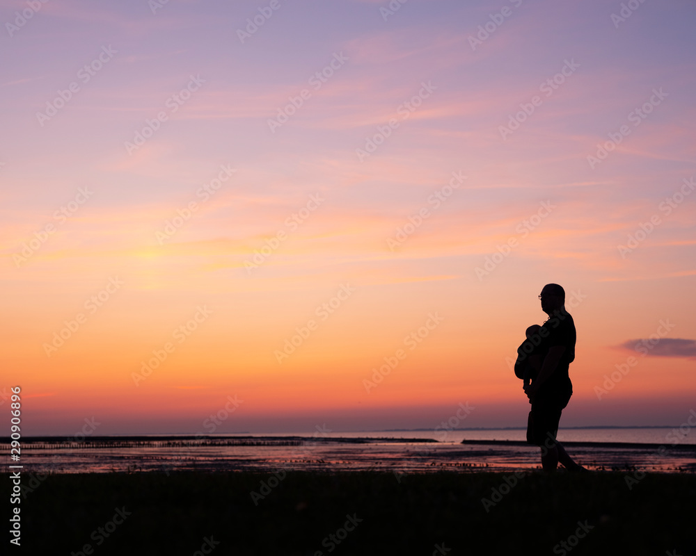 silhouette of man with child in baby carrier against colorful sunset