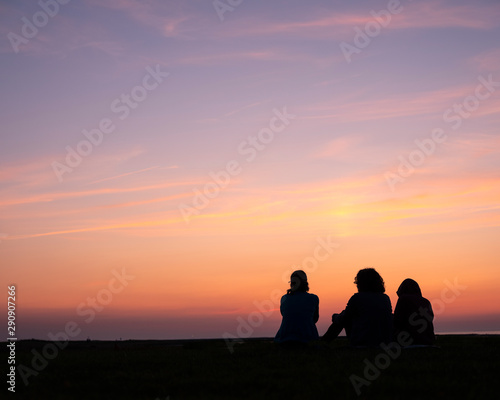 woman and two children sit watching colorful sunset