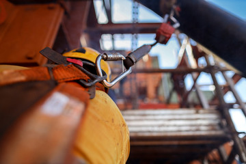 Side view of construction welder wearing safety helmet, fall arrest harness clipping retraceable device energy shock absorber lanyard on the back of his safety harness loop to preventing falling down 