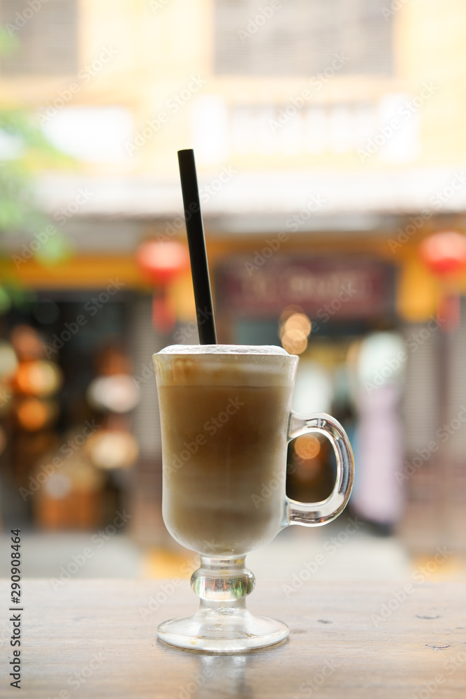 Empty tall transparent glass of macchiato or capuccino coffee with small white syrup mug and Vietnam money banknote and Vietnamese straw hat with traditional hat in coffee. Shop as background Empty tall transparent glass of macchiato or capuccino coffee with small white syrup mug and Vietnam money banknote and Vietnamese straw hat with traditional hat in coffee. Shop as background