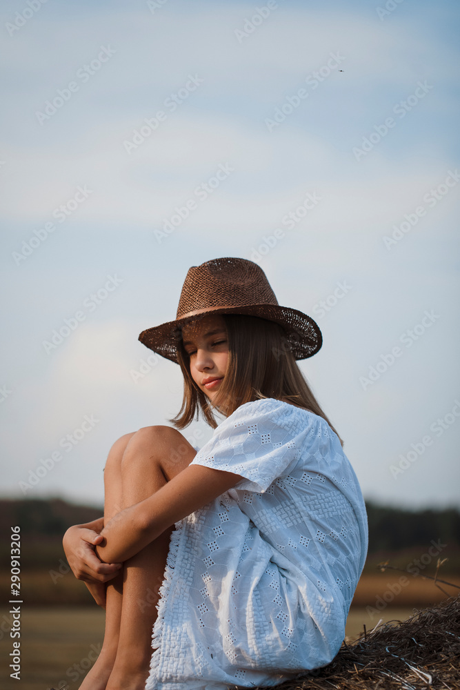 Little girl in a field with hay rolls at sunset