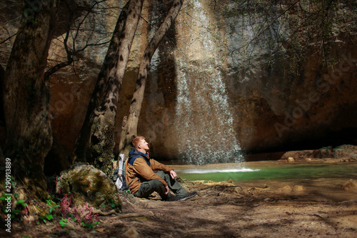 A red-haired man in a brown windbreaker and with a backpack sits near the Kozyrek (translation: Visor) waterfall, located in the Baydar Valley near the city of Sevastopol in Crimea.