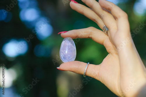 Female hand with transparent amethyst quartz yoni egg for vumfit, imbuilding or meditation. Shining crystal egg in hands on sky and sunrise background outdoors. Womens health concept. photo