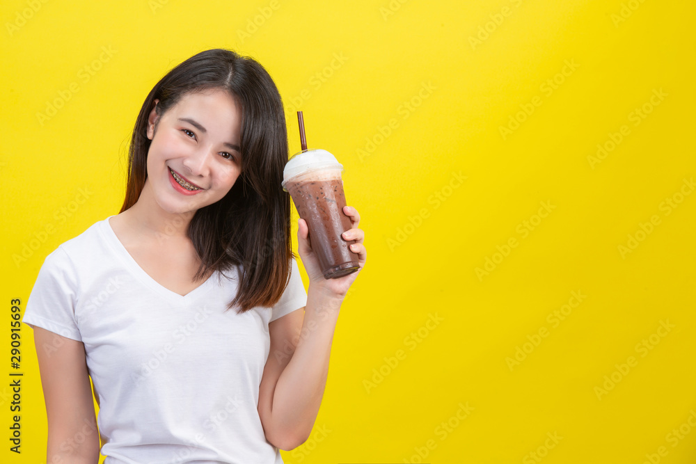 The girl drinks cold water from cocoa from a clear plastic glass on a yellow background. The girl drinks cold water from cocoa from a clear plastic glass on a yellow background.