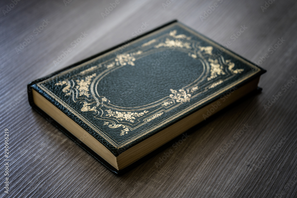 Antique book with green cover with golden decorations resting on the wooden table Antique book with green cover with golden decorations resting on the wooden table