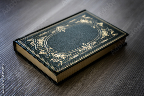 Antique book with green cover with golden decorations resting on the wooden table
