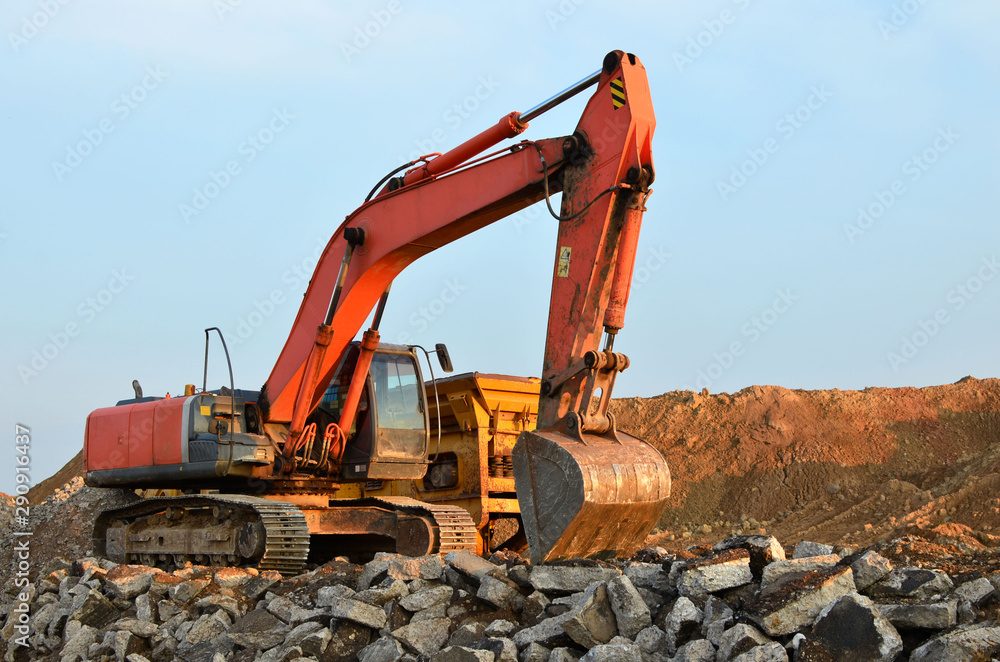 Heavy excavator working at gravel quarry unloads old concrete stones for crushing and recycling to gravel or cement. Special heavy construction equipment for road construction. Heavy excavator working at gravel quarry unloads old concrete stones for crushing and recycling to gravel or cement. Special heavy construction equipment for road construction.
