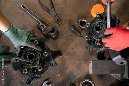 Hands wearing safety gloves repairing metal parts on a workshop bench - Overhead view of mechanics using hand tools to fix mechanical auto parts - Auto repair, industry and engineering concept