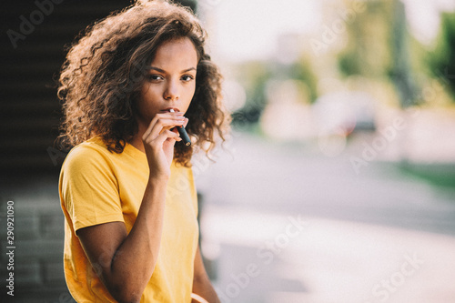Obraz na plátně Girl with curly hair smoking electric cigarette