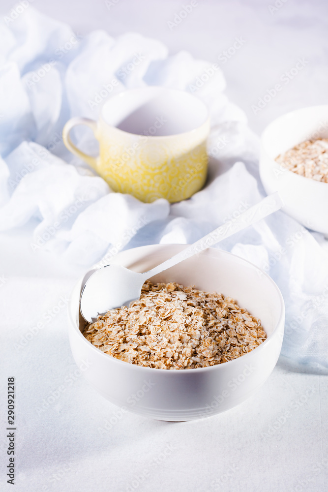 Raw oatmeal for making healthy breakfast in white ceramic bowl on light background. Top view. Raw oatmeal for making healthy breakfast in white ceramic bowl on light background. Top view.