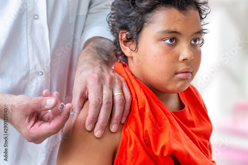 Childhood injection. 10-12r-old boyt watcing as vaccine,a drug is injected into her arm. by doctor photo