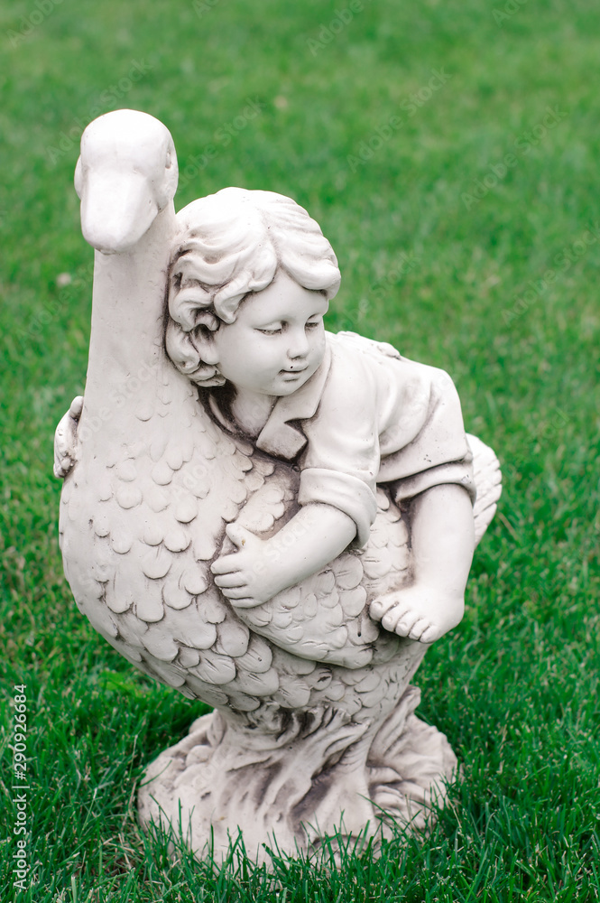 Garden figurine on green grass. Statuette of a girl on a goose. Garden figurine on green grass. Statuette of a girl on a goose.