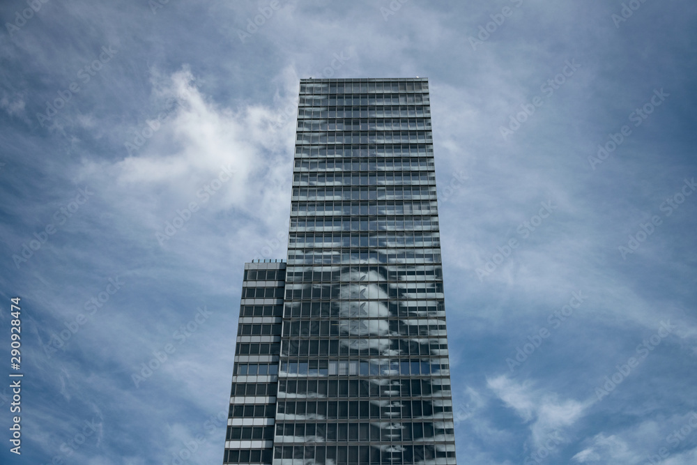 Single skyscraper against a blue sky with soft white clouds – symbol for economy, business, capitalism, banks and office spaces Single skyscraper against a blue sky with soft white clouds – symbol for economy, business, capitalism, banks and office spaces