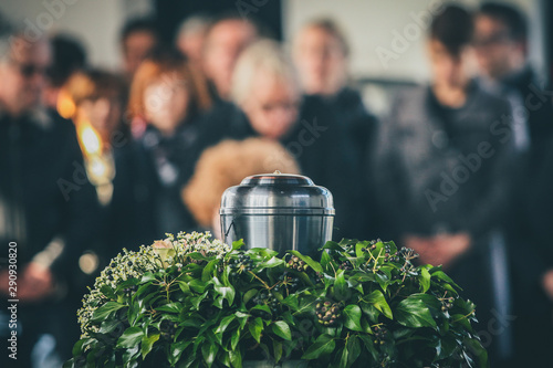 A metal urn with ashes of a dead person on a funeral, with people mourning in the background on a memorial service. Sad grieving moment at the end of a life. Last farewell to a person in an urn. photo