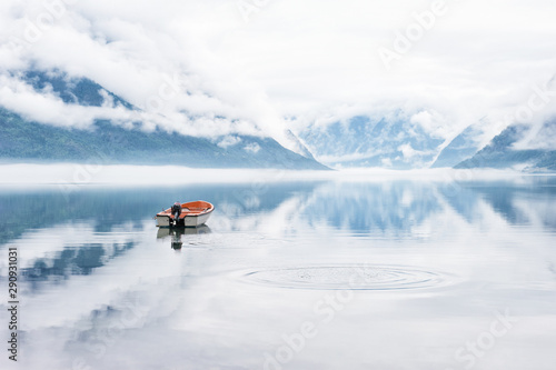 Beautiful landscape with fjord, boat and clouds reflected in the water, Norway