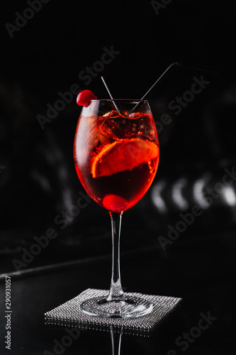 An orange cocktail in a wine glass with an orange slice and a cherry. Aperol spritz. Dark background.