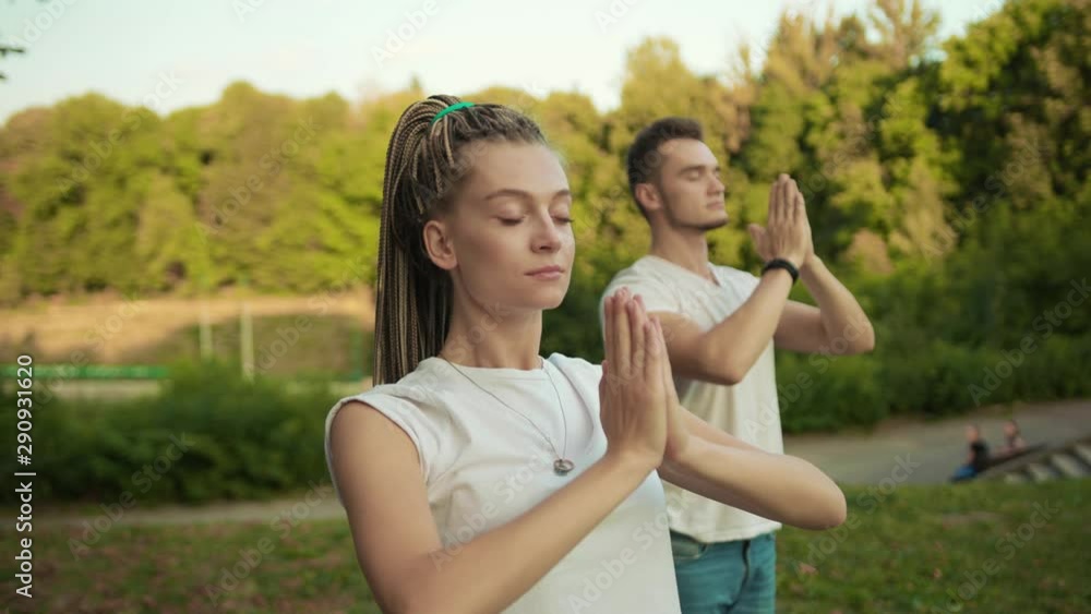 Caucasian hipster girl and her boyfriend training together in the park practising yoga asana poses exercises outside. Sport and health concept.