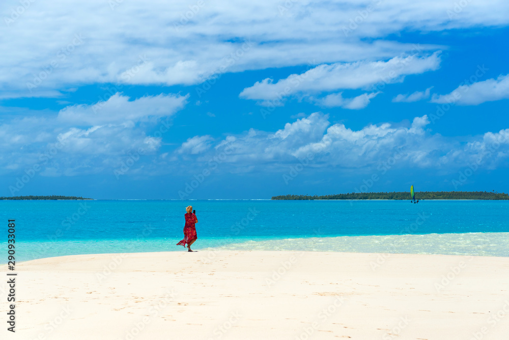 Woman in a red dress on the beach, Aitutaki island, Cook Islands, South Pacific. Copy space for text.