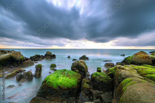 Green algae on rocks in the beach the dawn with dramatic sky to welcome the new day