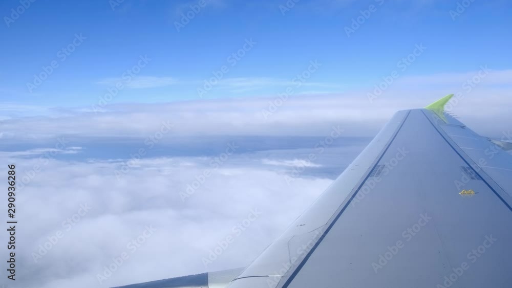 Wing of an airplane descending through thick clouds with a clear blue sky, an airplane landing. Wing of an airplane descending through thick clouds with a clear blue sky, an airplane landing.